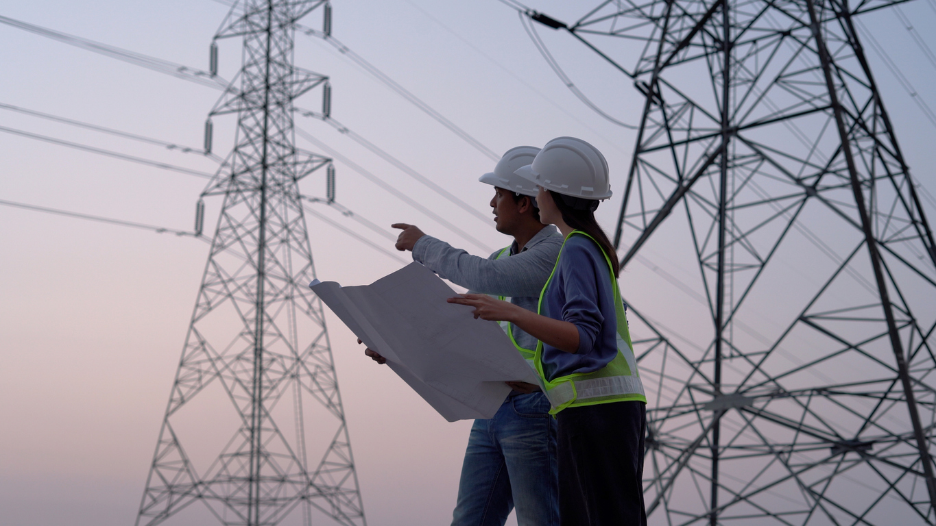 Dos personas con unos planos en la mano observando unas torres eléctricas