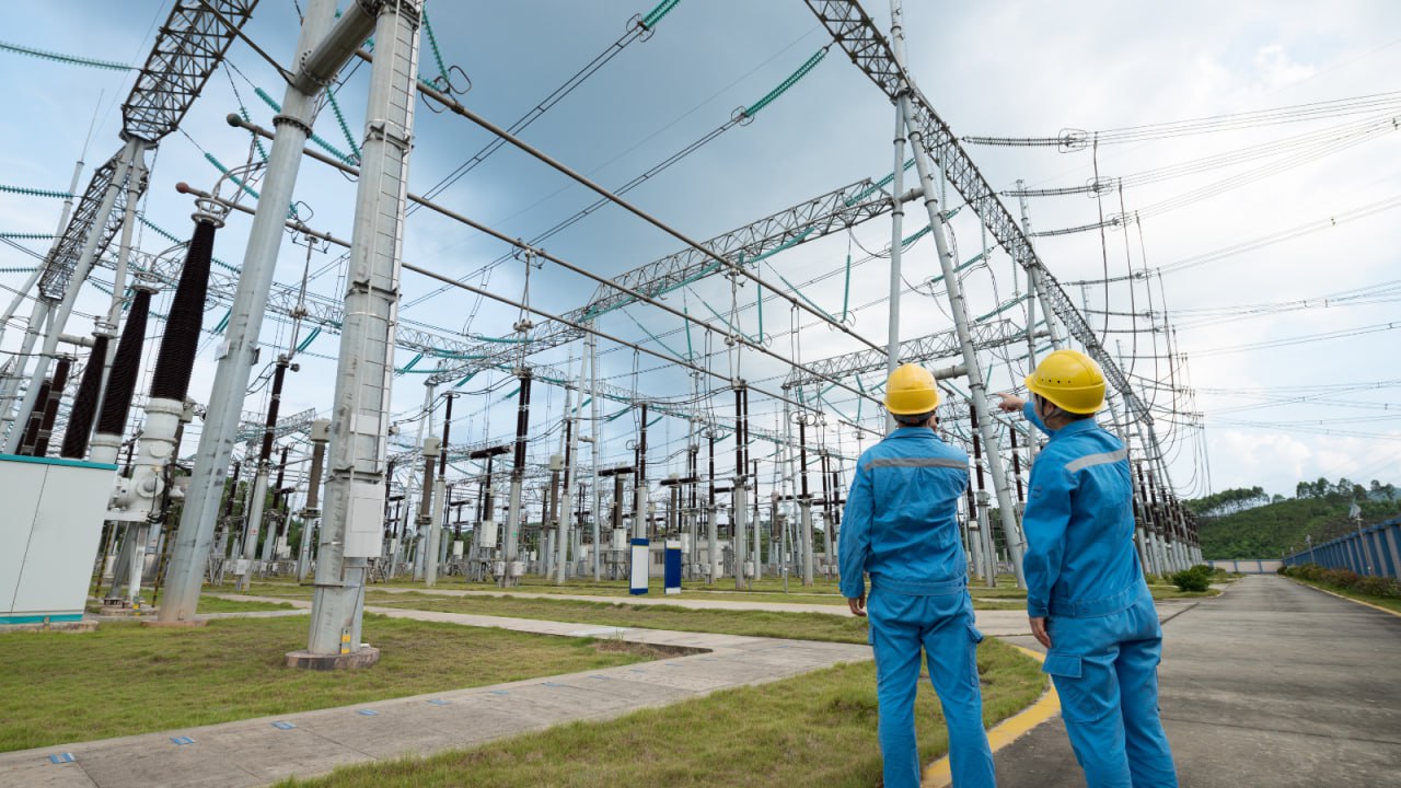 Dos personas con mono de trabajo y casco de obra revisando una instalación eléctrica