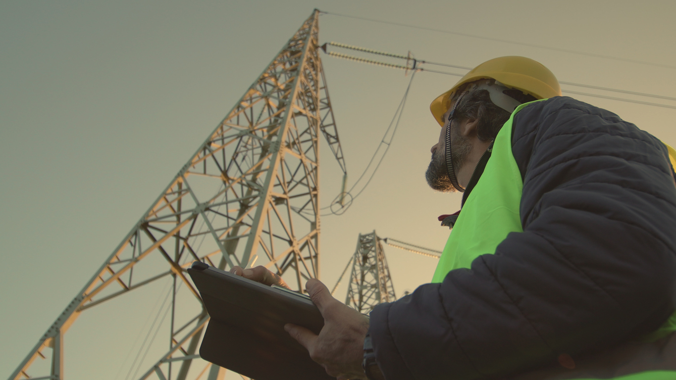 Hombre con casco y chaleco revisando una torre de alta tensión